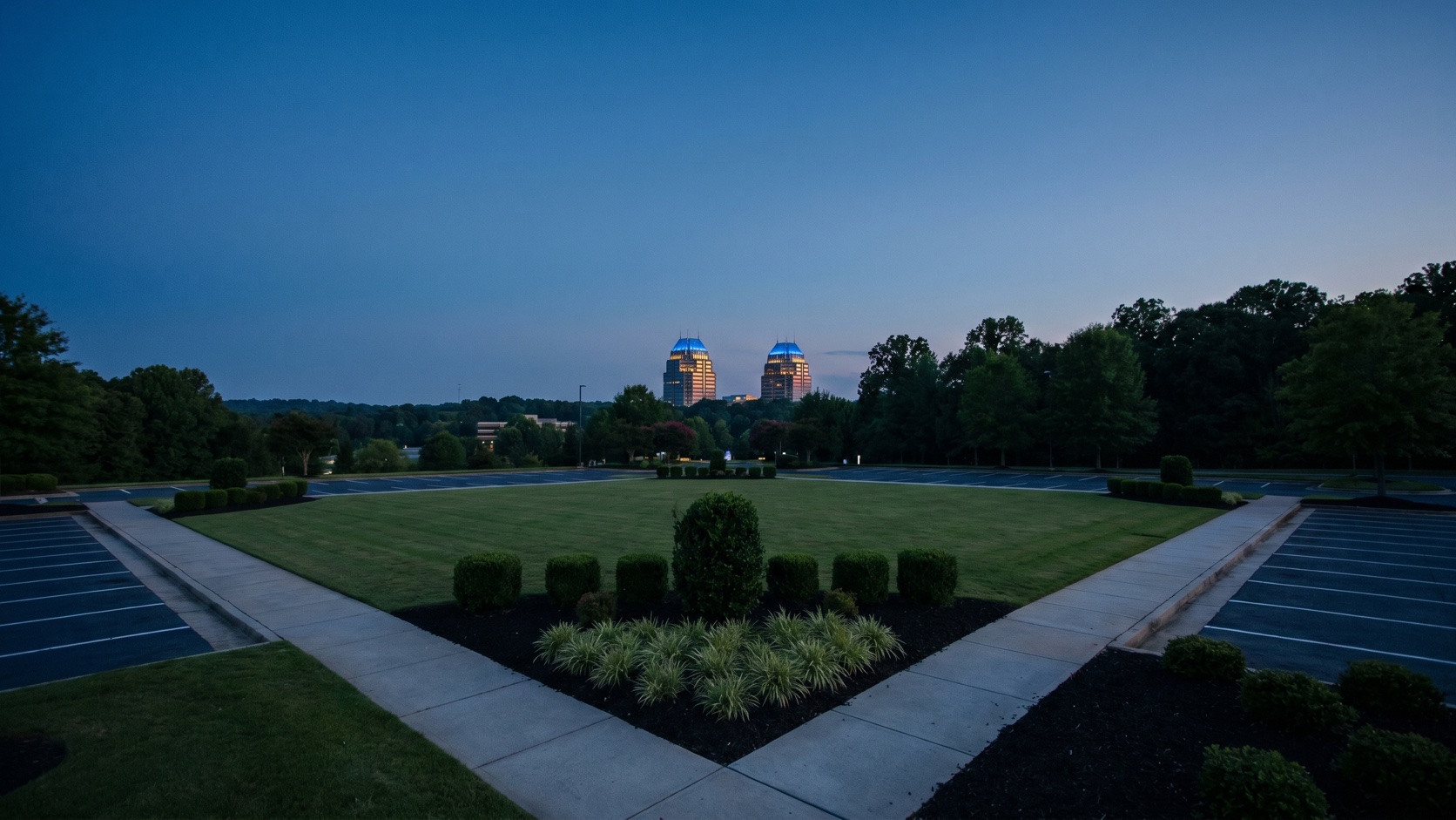 Manicured commercial office campus at dusk with the King and Queen towers of Sandy Springs rising beyond the tree line
